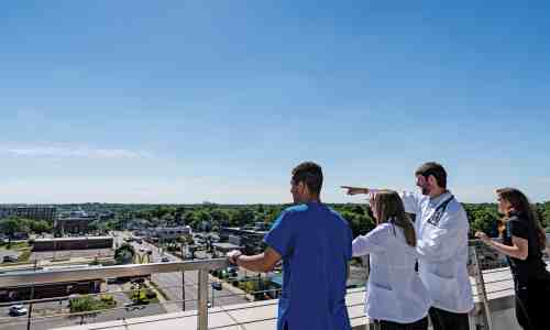 Three people stand on the outdoor patio overlooking medical mile